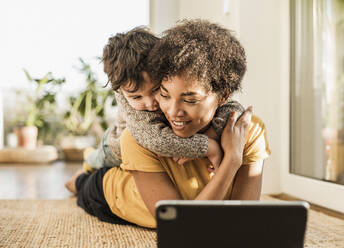 Smiling mother with son using digital tablet while lying at home - UUF22649