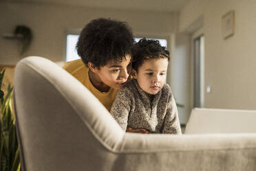 Young woman and boy using digital tablet while sitting on sofa at home - UUF22651