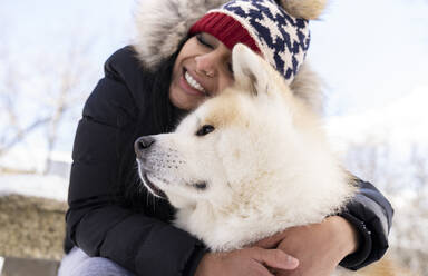 Glückliche Frau mit geschlossenen Augen umarmt Hund im Winter - JCCMF00849