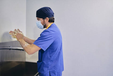 Male doctor wearing face mask washing hands while standing at hospital stock photo