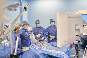 Surgeons in face mask and medical scrubs operating arthroscopic surgery while standing at operation room during COVID-19 - SASF00149