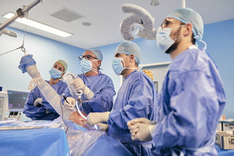 Chirurg mit Endoskopausrüstung bei einer Schulterarthroskopie im Stehen mit einem Kollegen im Operationssaal während COVID-19, lizenzfreies Stockfoto