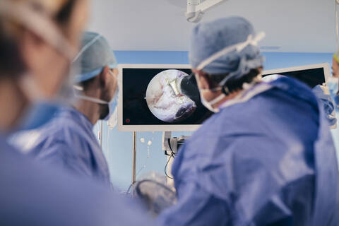 Fachleute, die im Operationssaal stehen und die Operation auf dem Computerbildschirm überwachen, lizenzfreies Stockfoto