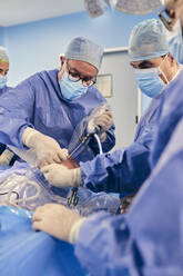 Älterer Arzt, der eine arthroskopische Operation an der Schulter mit einem Kollegen durchführt, während er im Operationssaal bei COVID-19 steht - SASF00159