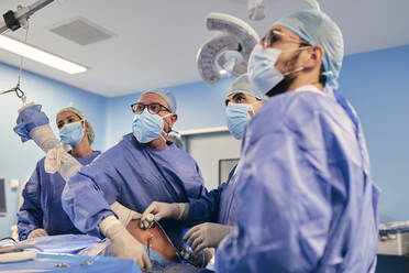 Fachkräfte, die eine arthroskopische Operation an der Schulter durchführen, während sie im Operationssaal bei COVID-19 stehen - SASF00162
