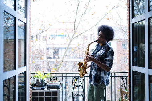 Afro-männlicher Musiker übt Saxophon auf dem Balkon zu Hause - JCMF01800
