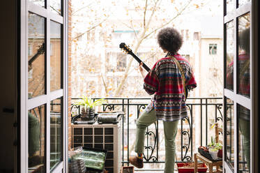 Junger Afroamerikaner übt Gitarre auf dem Balkon, gesehen durch eine Türöffnung - JCMF01803