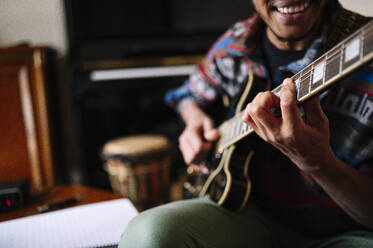 Lächelnder männlicher Musiker, der in einem Wohnzimmer Gitarre spielt - JCMF01808