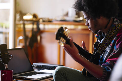 Afro male musician practicing guitar at home - JCMF01809