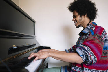 Lächelnder männlicher Musiker beim Üben am Klavier im Wohnzimmer - JCMF01814