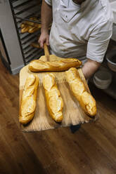 Männlicher Koch hält frisch gebackenes Baguette auf einer Pizzaschale in einer Bäckereiküche - JCMF01820