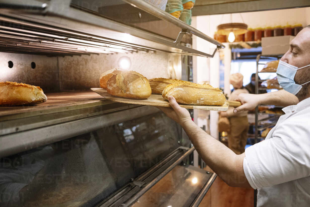 Baker taking out freshly baked bread from the oven of a bakery stock photo