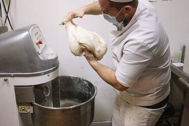 Erwachsener Koch bei der Zubereitung von Brotteig mit einem elektrischen Mixer in einer Bäckerei während COVID-19 - JCMF01838