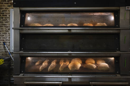 Loaf of breads being baked in oven at bakery - JCMF01840