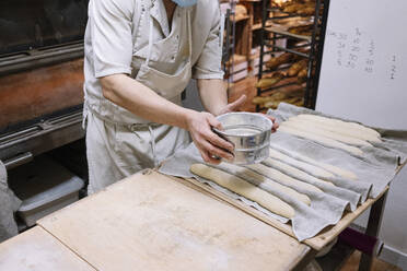 Männlicher Koch siebt Mehl aus einem Sieb auf den Teig in einer Bäckerei - JCMF01842