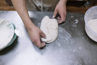 Mittlerer Erwachsener, der in einer Bäckerei an der Küchentheke Teig zubereitet - JCMF01844