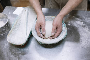 Männlicher Bäcker hält Mehlteig in einem Behälter in der Küche einer Bäckerei - JCMF01845