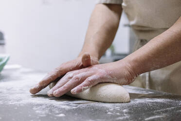 Männlicher Koch knetet Mehlteig auf dem Küchentisch in einer Bäckerei - JCMF01846