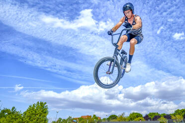 Junger Mann mit Fahrrad springt gegen blauen Himmel im Fahrradpark - GGGF00785