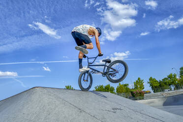 Young man performing stunt with bicycle on sports ramp at bike park - GGGF00790