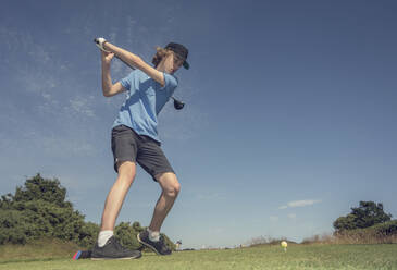 Jugendlicher schlägt Golf gegen den blauen Himmel auf dem Golfplatz - AJOF00980