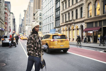 Rückenansicht einer Afroamerikanerin in stilvoller warmer Kleidung, die bei einem Spaziergang in New York die Straße überquert und über die Schulter schaut - ADSF19812