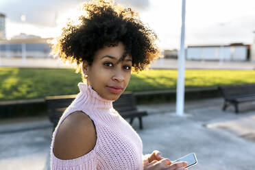 Schöne Frau mit lockigem Haar mit Smartphone gegen den Himmel - MGOF04648