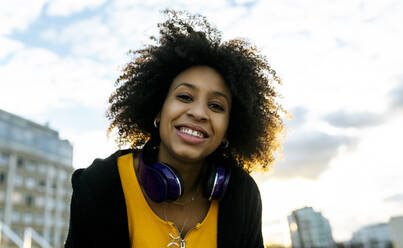 Lächelnde junge Frau mit Afro-Haar gegen den Himmel bei Sonnenuntergang - MGOF04657