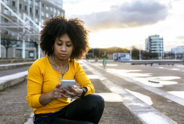 Beautiful woman listening music and using smart phone while sitting on steps - MGOF04660