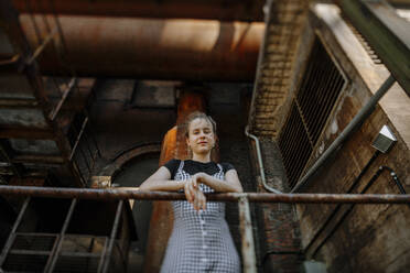 Teenager-Mädchen steht am Geländer eines verlassenen Gebäudes - OGF00781
