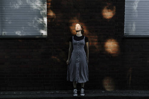 Teenage girl with eyes closed standing against brick wall - OGF00783