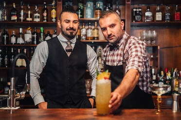 Bärtige Barkeeper lächelnd bei der Zubereitung frischer Cocktails am Tresen einer Bar - ADSF19842