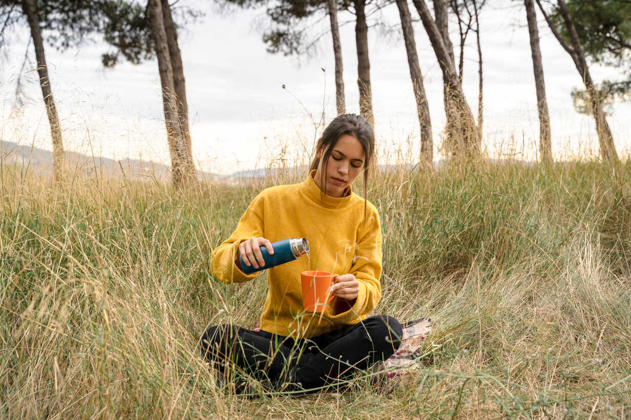 Woman is pouring hot drink from thermos into travel mug