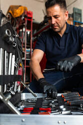 Vorderansicht eines männlichen Technikers, der bei der Arbeit in der Garage Schraubendreherbits aus dem Werkzeugkasten nimmt - ADSF19888