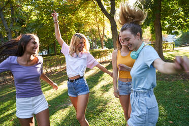 Group of laughing multiracial teen female friends having fun and dancing together while spending summer day in green park - ADSF19902