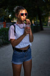 Hipster Teenagerin mit Sonnenbrille genießt kalten Milchshake beim Ausruhen im Park an einem Sommertag - ADSF19906
