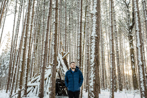 Mann schaut weg, während er gegen ein Holzzelt im Wald steht - AWAF00033