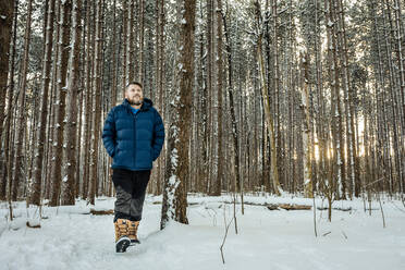 Mittlerer erwachsener Mann mit Händen in den Taschen, der beim Spaziergang im Wald wegschaut - AWAF00034