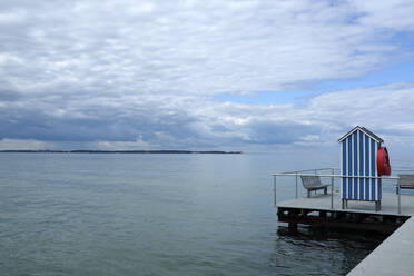 Deutschland, Schleswig Holstein, Stein, Steg mit blau-weißer Strandhütte an der Ostsee unter bewölktem Himmel - GISF00725