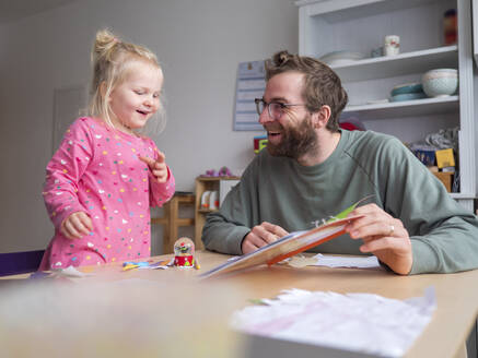 Glücklicher Vater zeigt seiner süßen Tochter ein Buch auf dem Tisch zu Hause - LAF02627
