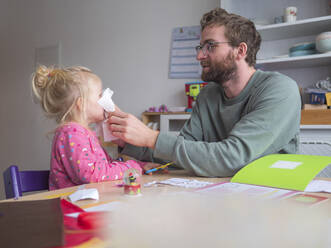 Verspielter Vater hält Papier an seine Tochter, während er am Tisch sitzt - LAF02628