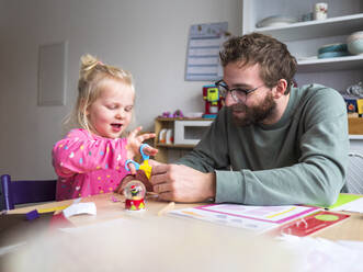 Vater und Tochter bei der Herstellung eines handwerklichen Produkts auf dem Tisch zu Hause - LAF02629