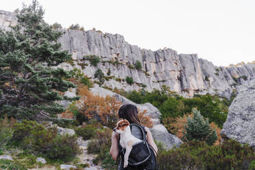 Frau mit Hund im Rucksack beim Wandern auf einem Berg - EBBF02180