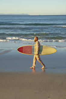 Mid adult man in suit walking with surfboard against sea - KBF00678