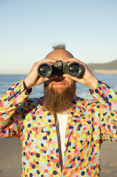 Mid adult man looking through binocular while standing at beach - KBF00682