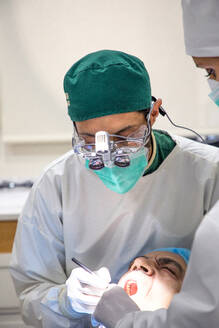 Fokussierter professioneller Zahnarzt, der die Zähne eines Patienten mit zahnärztlichen Instrumenten in einem hellen Raum in einer Klinik untersucht - ADSF19934