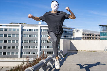 Mann mit Maske läuft an einem sonnigen Tag auf einem Dach - GGGF00794