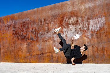 Young man holding face mask while dancing on footpath during sunny day - GGGF00801