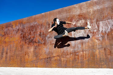 Young man jumping while dancing against brown wall - GGGF00808