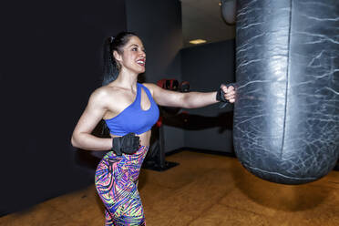 Lächelnde schöne Frau beim Training mit Boxsack im Fitnessstudio - GGGF00825
